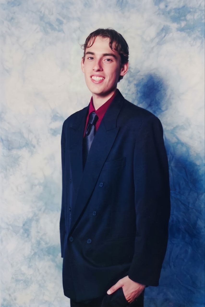 Mark Telfer, Year 12 graduation portrait, Mueller College, Rothwell. Navy double-breasted suit jacket, burgundy shirt, dark tie, studio backdrop.